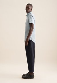 Lichtblauw kortemouwen geblokt shirt met een button-down kraag, gecombineerd met marineblauwe cropped broek en zwarte dress shoes.