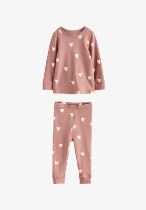 Roza pamučna pidžama sastavljena od majice dugih rukava i hlača s elastičnim pojasom, oboje ukrašeno bijelim uzorkom srca. Glatka tekstura i ležeran dizajn.