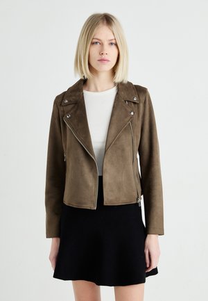 Veste de biker en daim marron avec fermeture éclair à l'avant, quincaillerie en argent, col à revers et silhouette ajustée, associée à un haut blanc et une jupe noire.