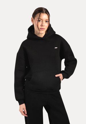 Sweat-shirt à capuche noire en tissu doux, avec une poche avant, des poignets côtelés et un petit logo sur la poitrine. Texture lisse dans l'ensemble.