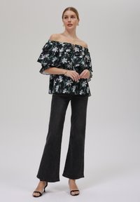 Off-shoulder svart blomstret bluse med lag av volanger, kombinert med høyt liv mørke flared jeans og svarte hælsandaler.