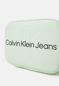 Prostokątne etui w mięcie, wykonane z teksturowanego materiału, z wytłoczonym logo "CK" i nadrukiem "Calvin Klein Jeans" pogrubioną czarną czcionką.