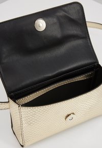 Kullanışlı bir bölme sunan açılabilir tasarıma sahip, pürüzsüz dokuya sahip ve gümüş bir çıtçıt kapanışı bulunan, siyah iç mekana sahip altın yılan desenli çanta.