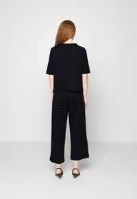 Top corto a maniche corte a scacchi neri e arancioni abbinato a pantaloni a gamba larga coordinati, caratterizzato da una vestibilità comoda e da un tessuto morbido, indossato con tacchi neri.