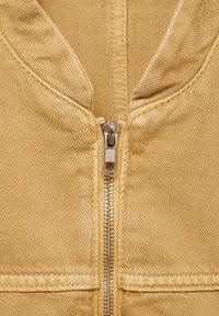 Gelbe Denim-Jacke mit Reißverschluss vorne, ausgestattet mit einer strukturierten Oberfläche und sichtbaren Nähten, die eine Nahaufnahme des Kragens und der Reißverschlussdetails zeigt.