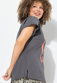 Camiseta gris de manga corta con un diseño gráfico en coral, que presenta una abertura lateral y un tejido suave y texturizado.