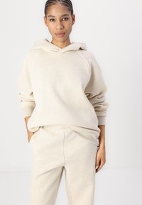 Beige Kapuzenpullover mit lockerer Passform, gerippten Bündchen und Nahtdetails, kombiniert mit passenden Sweatpants aus einem weichen, strukturierten Stoff.