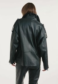 Czarna skórzana kurtka z wysokim kołnierzem, w luźnym kroju i zamkami na rękawach. Gładka tekstura i elegancki design, podkreślający zorganizowany styl.