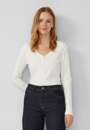 Witte geribde langemouwtop met een V-halslijn en knopen aan de voorkant, gecombineerd met donkere denim jeans met een klassiek vijf-pocketdesign.