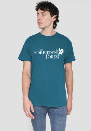 Young man with dark curly hair wearing teal t-shirt with "The Forbidden Forest" text and floral graphic, paired with blue jeans.