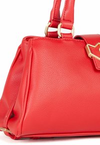 Bolso de mano de cuero rojo con forma estructurada, que presenta herrajes dorados, un acento en forma de corazón y una superficie texturizada. Dos asas cortas.