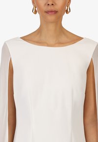 Robe blanche avec un col bateau et des manches courtes en tissu transparent. Des boucles d'oreilles en or en forme de créoles complètent le tissu doux et le design élégant.