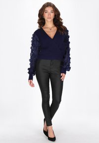 Laivastonsininen kietaisuneule, jossa teksturoidut röyhelöhihat; istuvat mustat leggingsit; malli käyttää mustia teräväkärkisiä kenkiä; sileä kangas, rento malli.