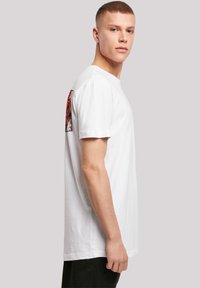 White cotton t-shirt with a round neckline and short sleeves, featuring a colorful graphic print on the left shoulder area.