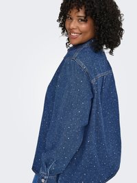 Camicia di jeans blu scuro con borchie argento, caratterizzata da una vestibilità comoda, colletto classico, maniche lunghe e polsini con bottoni, vista laterale.