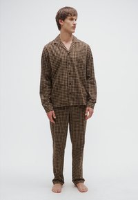 Brauner kariertes Pyjama-Set mit langen Ärmeln und Hose. Der Stoff wirkt weich und zeigt ein Hemd mit Knöpfen sowie einen elastischen Bund.