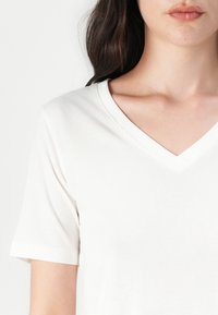 White cotton t-shirt with a V-neckline and short sleeves, featuring a smooth texture and minimal design. No visible patterns or accents.