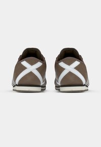 Ténis de camurça castanha com detalhes brancos, apresentando um padrão cruzado nas laterais, bico arredondado e sola de borracha.