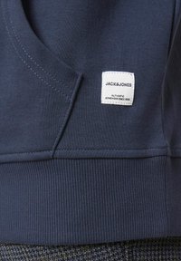 Navyblaues Sweatshirt mit weicher Textur, das ein Etikett mit "JACK&JONES" sowie gerippte Bündchen und Saum zeigt. Seitentaschendetails sichtbar.