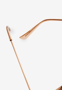 Gafas de sol color oro rosa con un delgado marco de metal y patillas curvas. Presentan un sutil detalle grabado a lo largo del brazo. Textura suave en toda su superficie.