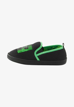 Zapatillas negras de andar por casa sin cordones con acentos verdes, que presentan un diseño gráfico texturizado en verde y negro en la parte frontal y un patrón de tablero de ajedrez en el interior.