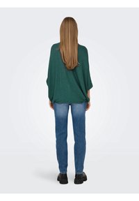 Haut en maille verte oversize avec une finition texturée, associé à un jean slim bleu clair et des chaussures à plateforme noires.