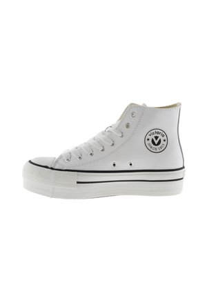 Sneaker bianca alta con allacciatura frontale, suola in gomma e patch con logo Victoria sulla caviglia su sfondo bianco.