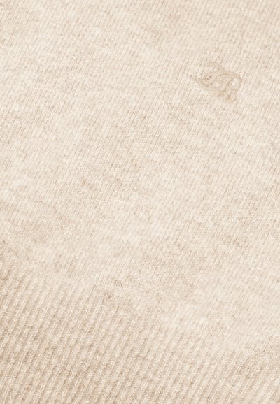 Tessuto a maglia beige con una consistenza morbida e un motivo a coste. Presenta un logo sottile, leggermente embossato, che si fonde con il materiale.