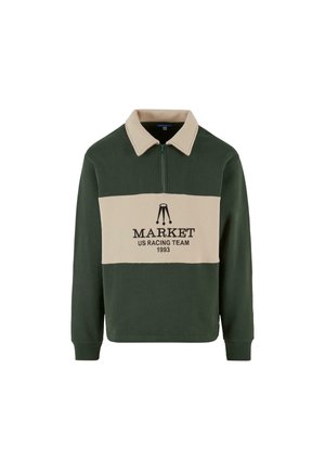 Zielona i beżowa longsleeve polo bluza z zamkiem przy kołnierzu, z napisem "MARKET US RACING TEAM 1993" nadrukowanym na środku na czarno.