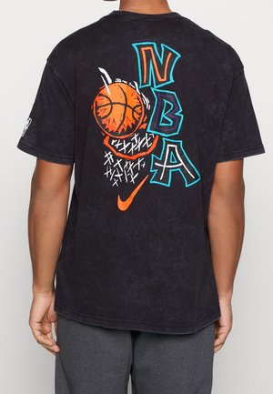 Osoba nosząca czarną koszulkę NBA z kolorową grafiką przedstawiającą piłkę do koszykówki i obręcz oraz pomarańczowe logo Nike na plecach.