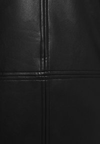 Gros plan d'une surface en cuir noir avec des coutures verticales et horizontales détaillées qui se croisent formant un motif en croix.