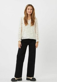 Hvid blondebluse med lange, puffede ærmer, parret med sorte bredde bukser og chunky sorte sandaler. Enkel design med teksturerede detaljer.