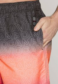 Feketéből pirosba átmenő színű úszónadrág, amelyen a "DAvid Camp" minta ismétlődik. Oldalsó zsebbel és rugalmas derékkal rendelkezik.