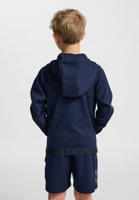 Mörkblå hoodie med huva, tillverkad av mjukt material, med en bakre design och figurnära midja. Kombinerad med matchande shorts och logodetaljer.