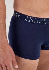 Navy blue boxer briefs made of soft fabric, featuring a white branded elastic waistband with a smooth texture and a snug fit.
