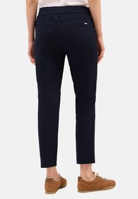 Pantaloni blu navy con vita elasticizzata, design slim-fit, tasche posteriori e dettagli di cucitura discreti, abbinati a scarpe casual marroni.