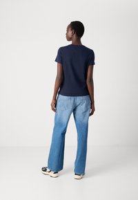 T-shirt navy a maniche corte in cotone, abbinato a jeans a gamba larga blu chiaro. L'outfit presenta un design minimalista e una vestibilità casual.