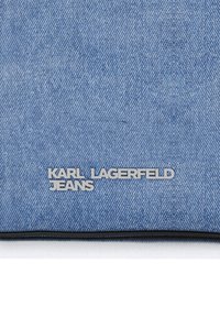 Μπλε τζιν ύφασμα με ασημί μεταλλικό λογότυπο "KARL LAGERFELD JEANS" κοντά στην κάτω άκρη, σε λευκό φόντο.