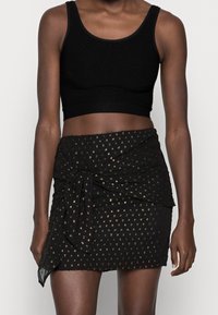 Black cropped tank top with ribbed texture, paired with a black wrap skirt featuring gold dot patterns and a twisted front detail.