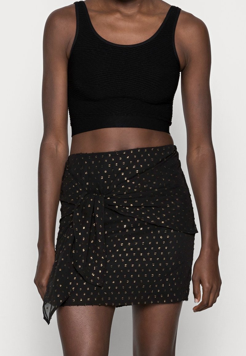 Black cropped tank top with ribbed texture, paired with a black wrap skirt featuring gold dot patterns and a twisted front detail.