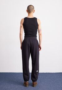 Black ribbed tank top, paired with dark sweatpants featuring an elastic waistband and gathered cuffs. Brown chunky shoes with rounded edges.