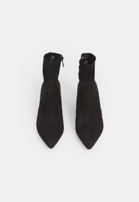 Une paire de bottines en nubuck noir avec des pointes effilées et des fermetures éclair sur les côtés, montrées de haut sur un fond blanc.