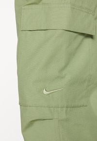 Ljusgröna cargobyxor med en texturerad yta, som har en framficka och en metallisk Nike-logotyp broderad på sidan.