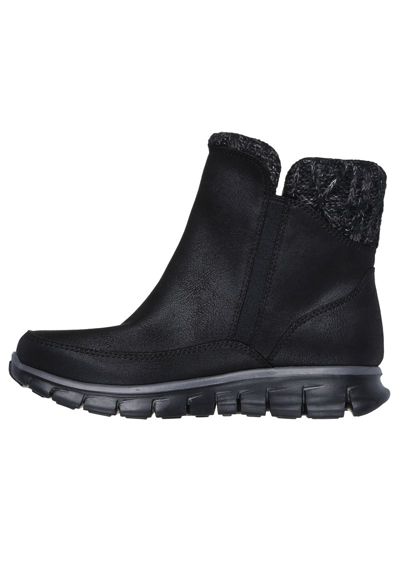 Botas negras de tobillo hechas de material sintético con un collar de punto texturizado, punta curvada y una suela de goma gruesa y segmentada.