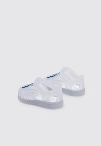 Sandali di plastica trasparente con un design traslucido, cinturini regolabili e suole interne decorate con motivi marini blu.
