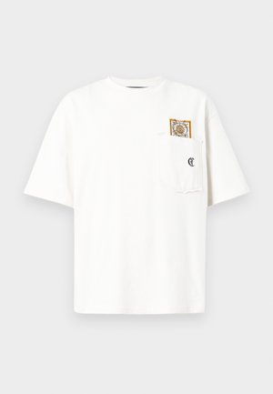 T-shirt bianca a maniche corte con una tasca sul petto che presenta un piccolo logo nero e una carta decorativa parzialmente inserita nella tasca.