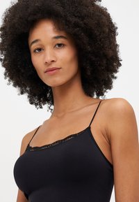 Top in raso nero con spalline sottili e rifinitura in pizzo lungo il collo. Realizzato in tessuto morbido. Design semplice e aderente senza ulteriori decorazioni.