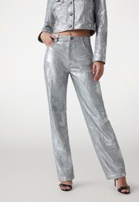 Giacca corta in metallo argento e pantaloni a vita alta con motivi a foglia in rilievo; texture liscia; abbinati a tacchi neri con cinturini.