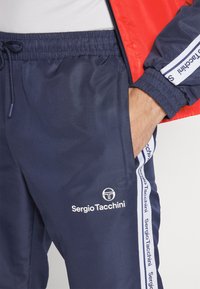 Jūras spēku sporta bikses ar teksturētu virsmu, elastīgu jostasvietu un sānu kabatām. Malās ir balta zīmola druka.