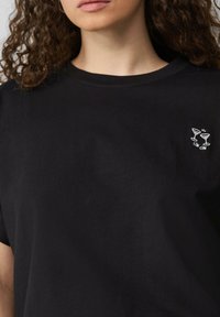 T-shirt en coton noir avec un col rond et des manches courtes, orné d'un petit motif brodé blanc représentant deux verres à cocktail et du texte "CIN CIN."